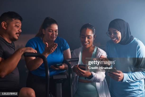 shot of a group of young people using smartphones while working out with exercise bikes in a gym - peloton app stock pictures, royalty-free photos & images