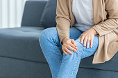 Woman suffering from knee pain sitting sofa in the living room, Mature woman suffering from knee pain while sitting on the sofa
