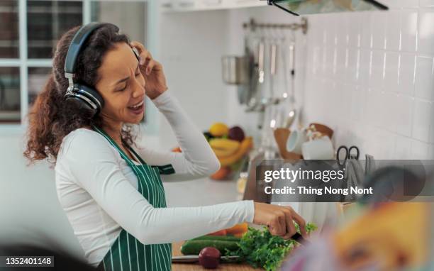 happy young woman housewife dancing alone cooking meal in modern kitchen. positive girl having fun with kitchen utensil at home. - stereotypical housewife ストックフォトと画像