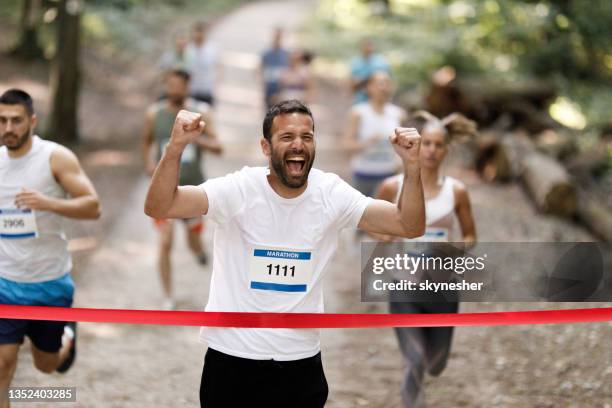 exitoso corredor de maratón cruzando la línea de meta con los brazos en alto. - carrera de carretera fotografías e imágenes de stock