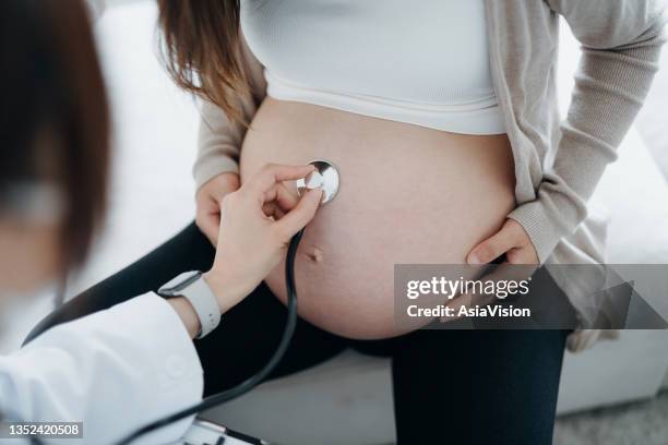 close up of a female doctor doing checkup on an asian pregnant woman, examining the belly with stethoscope. prenatal exam. pregnancy health and wellbeing concept - obstetrician 個照片及圖片檔