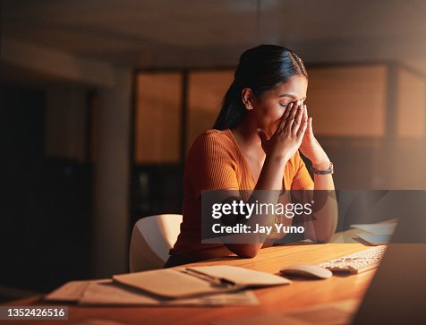 Foto de una atractiva joven empresaria sentada sola en la oficina por la noche y sintiéndose estresada Foto de una atractiva joven empresaria sentada sola en la oficina por la noche y sintiéndose estresada