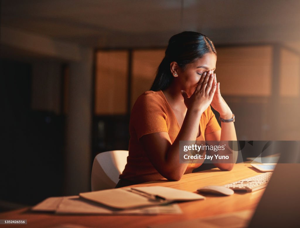 Shot of an attractive young businesswoman sitting alone in the office at night and feeling stressed