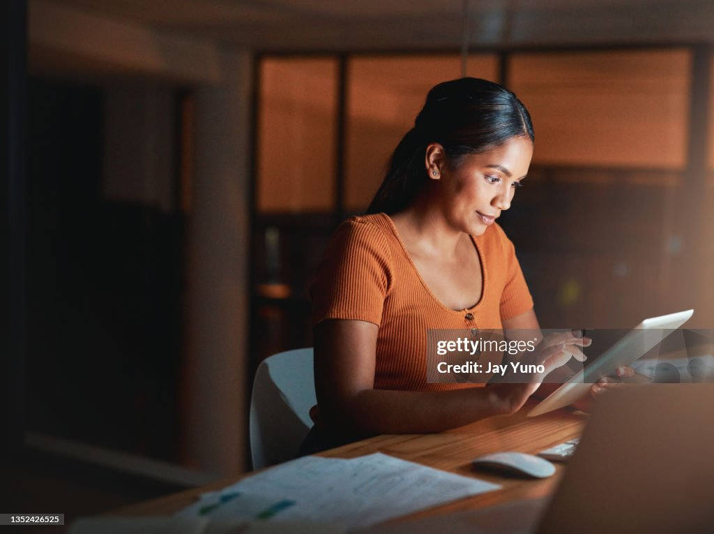 Shot of an attractive young businesswoman sitting alone in the office at night and using a digital tablet