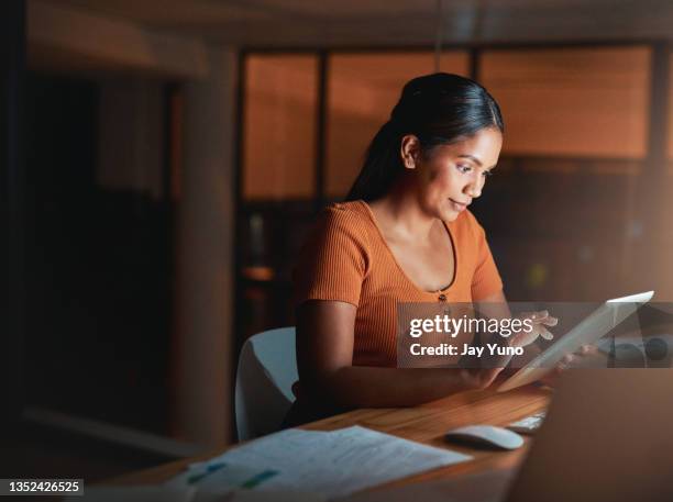 shot of an attractive young businesswoman sitting alone in the office at night and using a digital tablet - laptop stockfoto's en -beelden