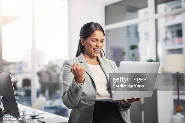 foto de una atractiva joven empresaria de pie en la oficina y celebrando un éxito mientras usa una computadora portátil - entusiasmo fotografías e imágenes de stock