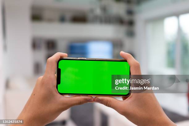 smartphone green screen in hands indoors - chroma key stock-fotos und bilder