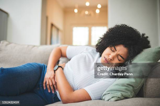 shot of a young woman holding her stomach in discomfort on the couch at home - woman holding tummy bildbanksfoton och bilder