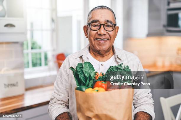 shot of a elderly man holding a grocery bag in the kitchen - alimentação saudável imagens e fotografias de stock