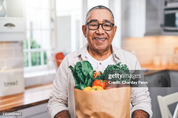 shot of a elderly man holding a grocery bag in the kitchen - hälsosamt ätande bildbanksfoton och bilder
