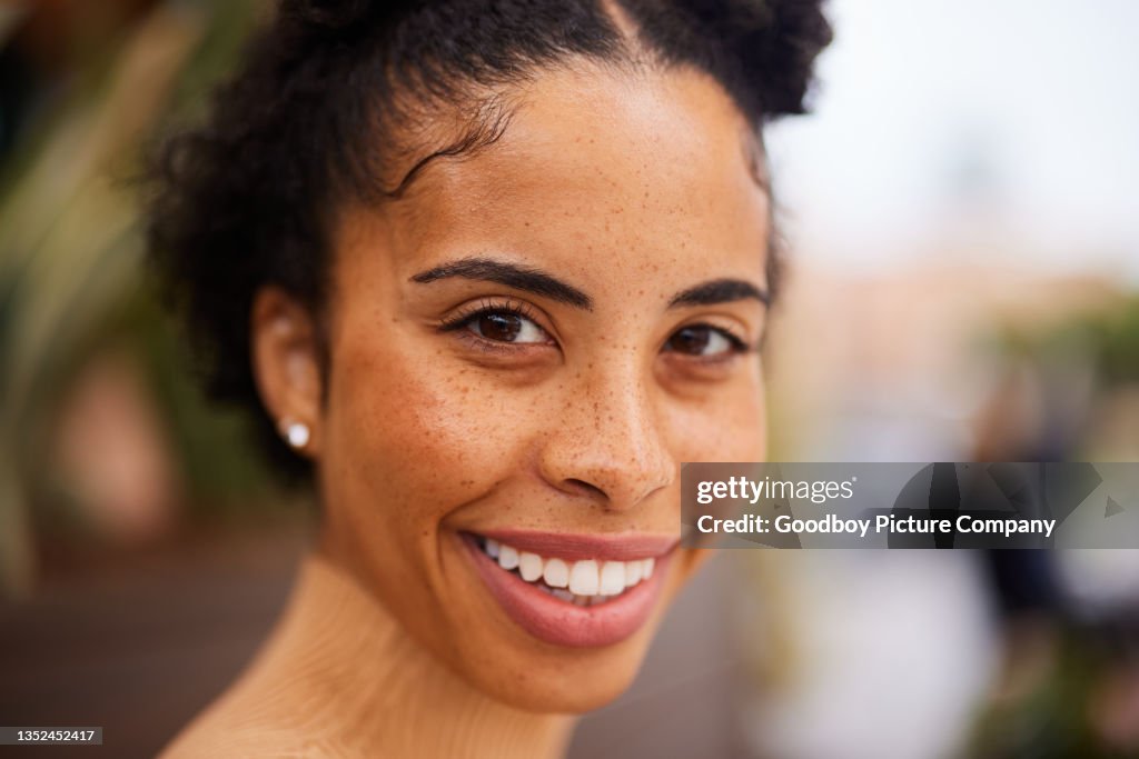 Young woman with freckles standing outside in summer and smiling