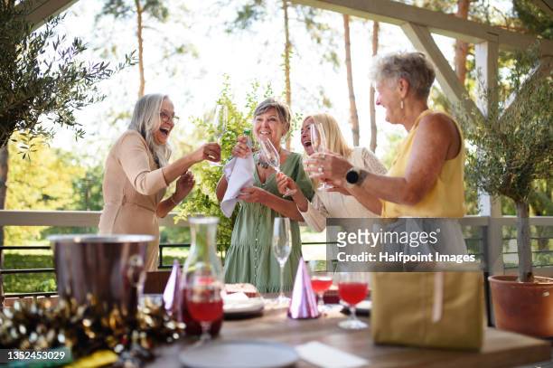 senior women friends opening champagne during celebration outdoors at hotel terrace. - hotel opening party stock pictures, royalty-free photos & images