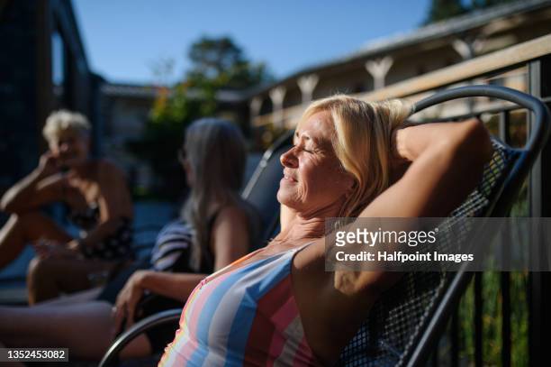 happy senior woman in swimsuit with her friends sunbathing outdoors in hotel resort. - senior women pool stock pictures, royalty-free photos & images