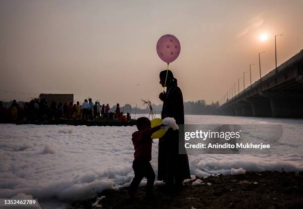 Hindu devotee holds a balloon as she stands next to the banks of River Yamuna amid toxic foam caused by pollution on the occasion of Chhat puja on...