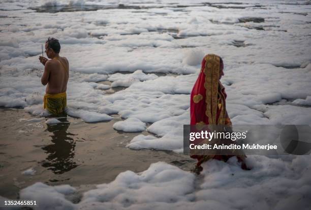 Hindu devotees perform a prayer ritual after taking a dip in the waters of River Yamuna amid toxic foam caused by pollution on the occasion of Chhat...