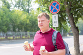 An adult man prone to fatness with two glasses of ice cream on a sunny day on a city street
