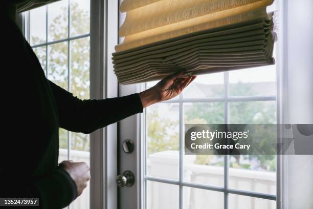 woman adjusts roman shade on french door - tapparelle foto e immagini stock