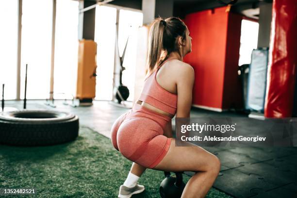 athletic female testing squat capabilities with kettlebell in gym - nádega imagens e fotografias de stock