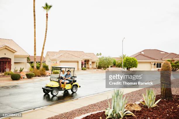 Extreme wide shot of couple driving electric golf cart on street in retirement community