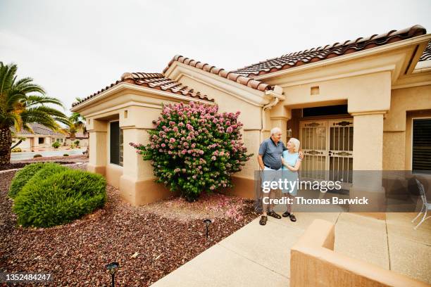 wide shot of smiling embracing senior couple standing in front of home in retirement community - arizona house stock-fotos und bilder