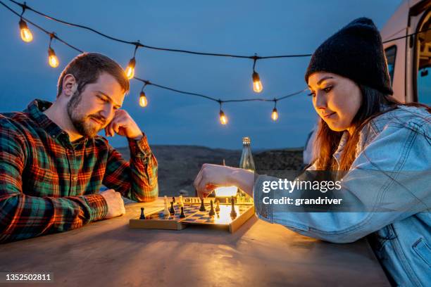 young couple out camping playing chess together at a picnic table - camping games stockfoto's en -beelden