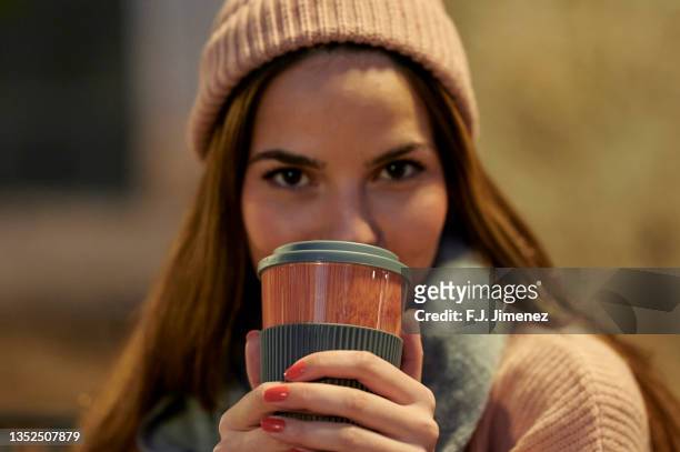 close-up of woman with hot take away drink on the street at night - tea outdoor stock-fotos und bilder