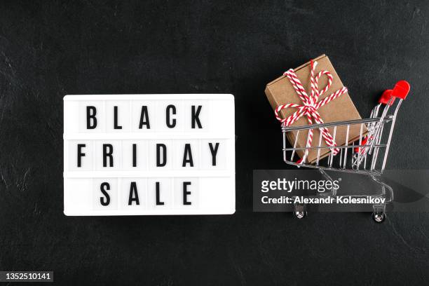 lightbox with text black friday sale, grocery cart with gift present on dark background - light box stock pictures, royalty-free photos & images