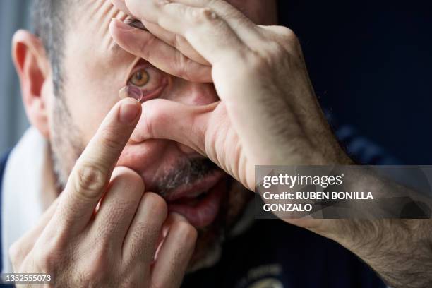 front view of mid adult caucasian man putting on a contact lens in eye. healthcare and medicine concept. - gonzalo caballero fotografías e imágenes de stock