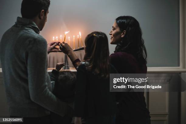 rear view of family lighting menorah during hanukkah - giudaismo foto e immagini stock