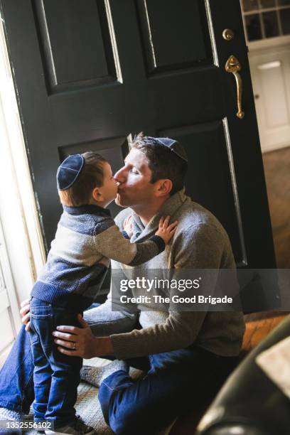 boy kissing father in doorway at home - gorra a modo de casquete fotografías e imágenes de stock