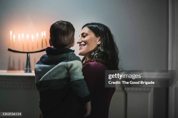mother and young son looking at menorah in living room at home - chanoeka stockfoto's en -beelden