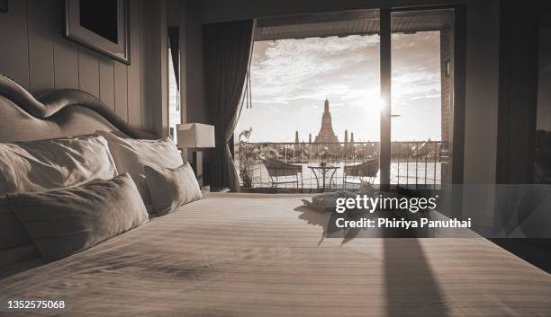 suite room with chaophraya river view and wat arun temple on background. temple of dawn and bangkok city in suite river view room decorated with a contemporary wooden decor and features natural hues and modern thai design. - bangkok hotel stock pictures, royalty-free photos & images