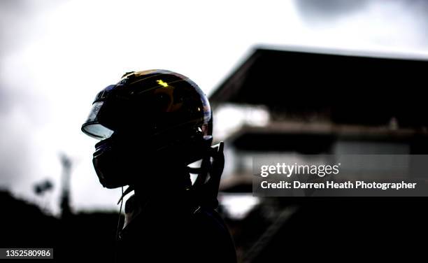 Photographed in silhouette Australian Red Bull Racing Formula One team racing driver Mark Webber walking along the pit lane wearing his crash helmet,...