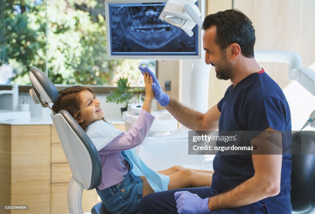 Nahaufnahme porträt eines männlichen Zahnarztes, der dem kleinen Mädchen in der Zahnklinik ein High Five gibt