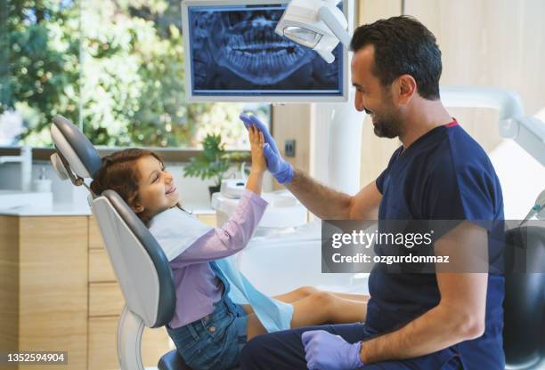 close up portrait of a male dentist giving a high five to little girl at dental clinic - dentist stock pictures, royalty-free photos & images