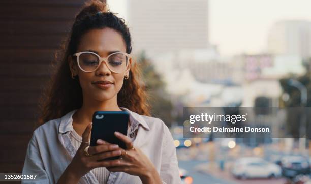 shot of an attractive young businesswoman texting while standing outside on the office balcony - woman with smartphone stockfoto's en -beelden