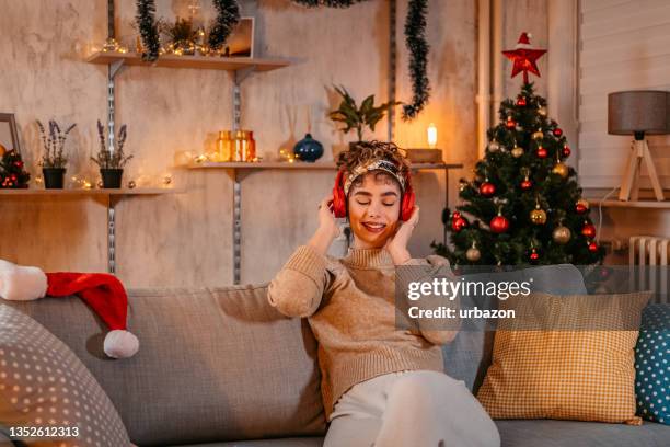 woman listening music on couch at christmas time - christmas music listen stock pictures, royalty-free photos & images
