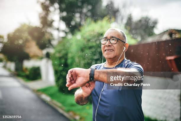 shot of a senior man standing alone outside and checking his watch after going for a run - fit for use stockfoto's en -beelden