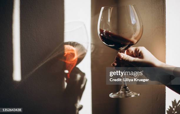 a woman's hand holding a glass of red wine. - rode wijn stockfoto's en -beelden