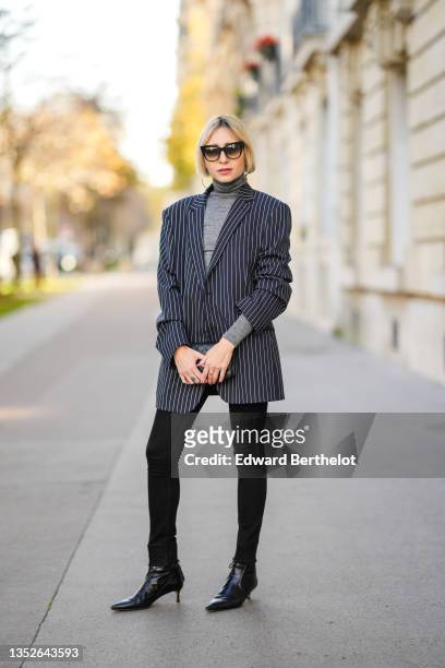 Emy Venturini wears sunglasses from Dita, large silver earrings, a gray wool turtleneck pullover from Intimissimi, a black with small white striped...