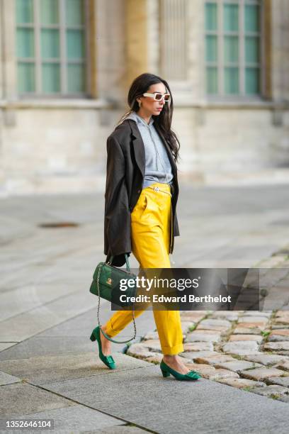 Gabriella Berdugo wears white sunglasses, a black oversized blazer jacket, a pale gray hoodie wool sweater, a green shiny leather Trendy handbag from...