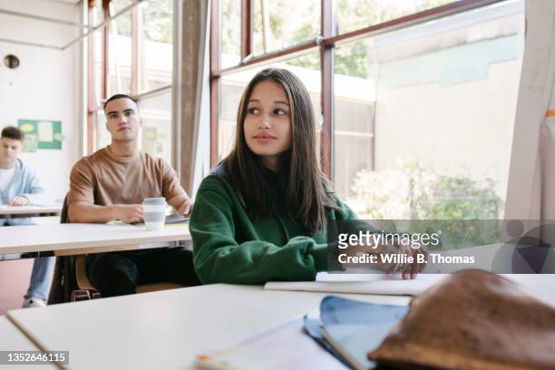 high school student sitting at desk by window in classroom - teacher desk foto e immagini stock