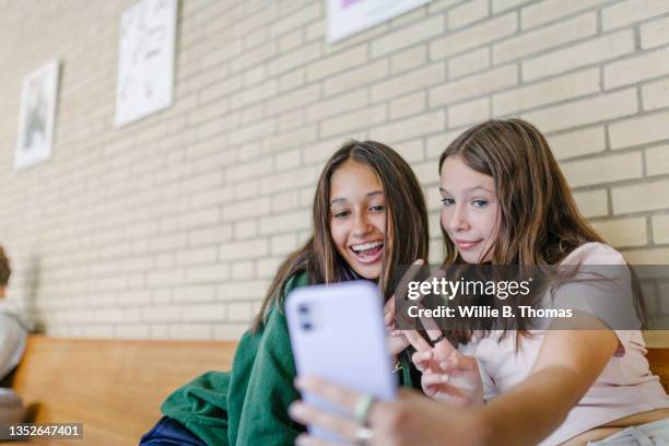 two girl friends taking selfie while waiting for class in high school - girl mobile stock-fotos und bilder