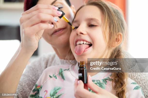 daughter sticking out tongue to mother can drop cbd oil drops on it - cannabidiol stock pictures, royalty-free photos & images