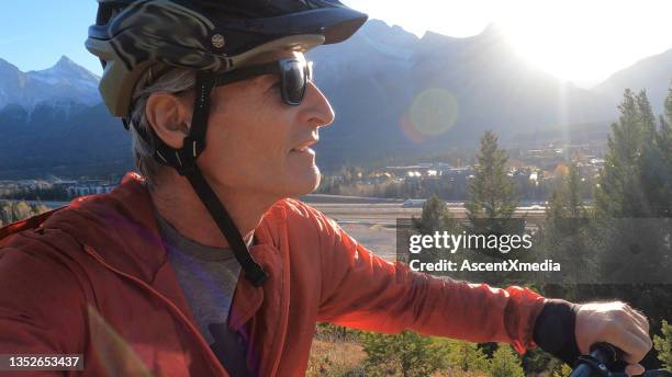 retrato de un hombre maduro en bicicleta de montaña sobre el valle al atardecer - sunglasses overhead fotografías e imágenes de stock