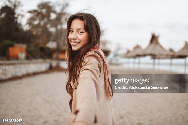 smiling female leading you to explore autumn beach tranquility with her - alleen één tienermeisje stockfoto's en -beelden