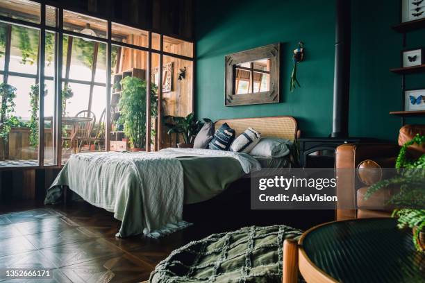 a stylish loft bedroom interior with brown coloured rattan furniture and wooden elements with dark green coloured wall. decorated with plants - king size bed stockfoto's en -beelden