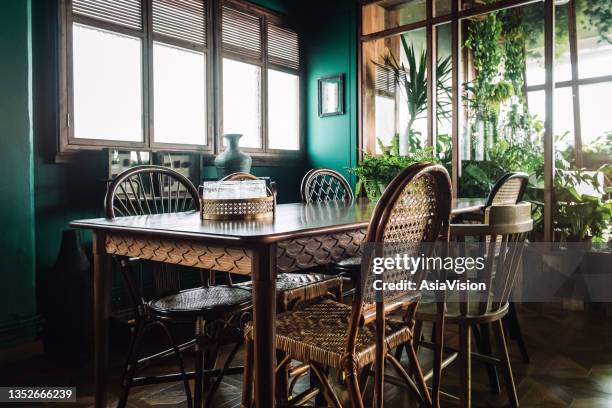 a stylish dining room interior with brown coloured rattan furniture and wooden elements with dark green coloured wall. decorated with plants - dining room stock pictures, royalty-free photos & images