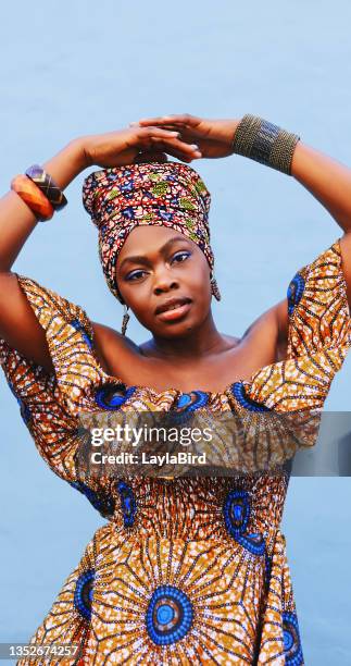 portrait of a beautiful young woman wearing traditional african clothing against a blue background - head tie stock pictures, royalty-free photos & images