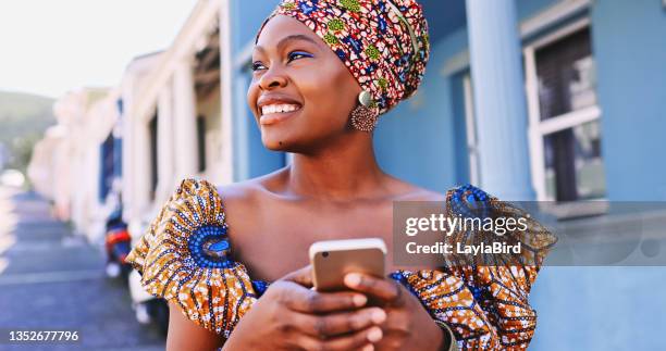 aufnahme einer schönen jungen frau in traditioneller afrikanischer kleidung und mit einem smartphone vor einem urbanen hintergrund - traditionelle kleidung stock-fotos und bilder